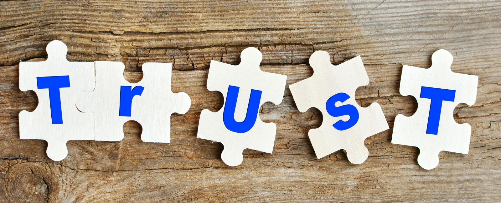 Puzzle pieces spelling the word TRUST on wooden background symbolizing confidence and reliability