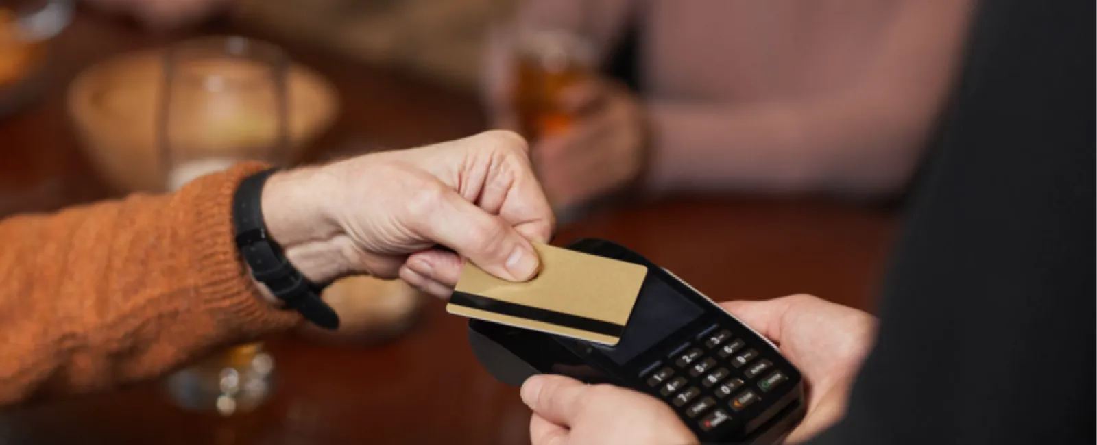 Person paying with contactless credit card on a payment terminal at a wooden table in a social setting