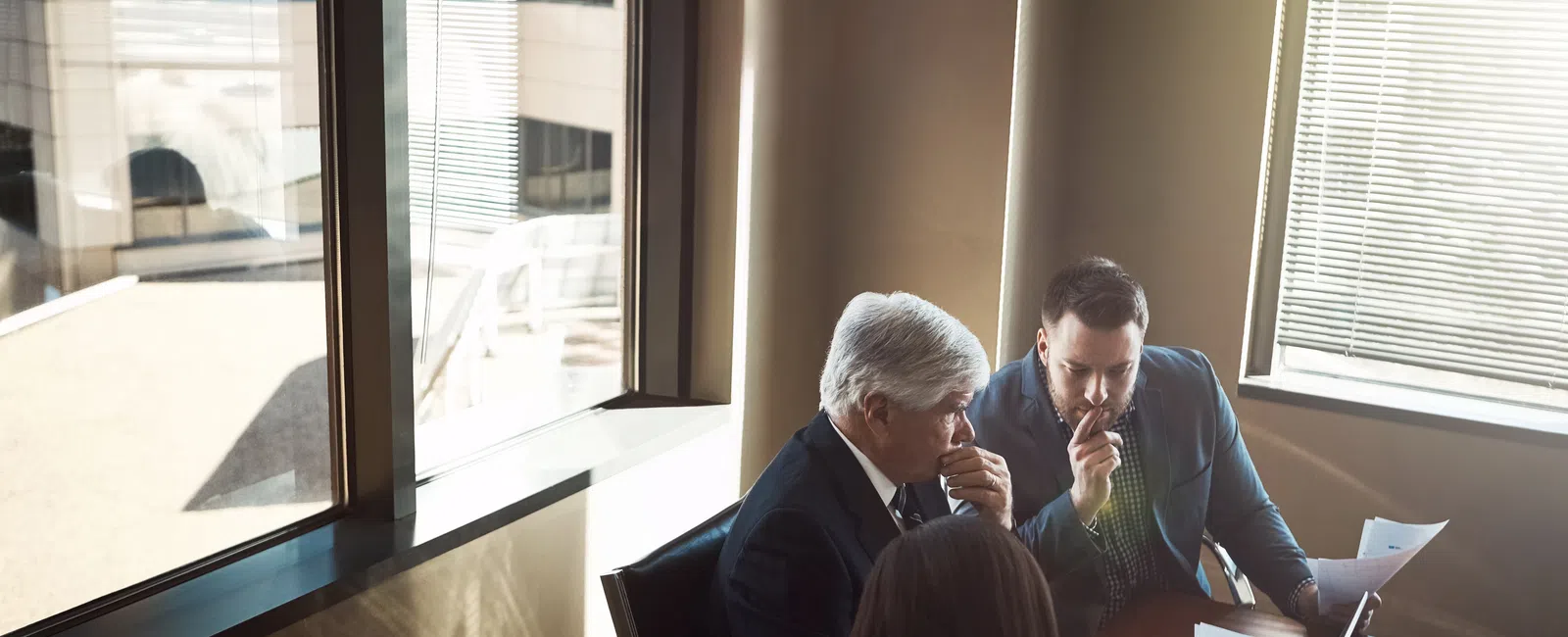Three business professionals engaged in a focused discussion around a laptop in a sunlit office.
