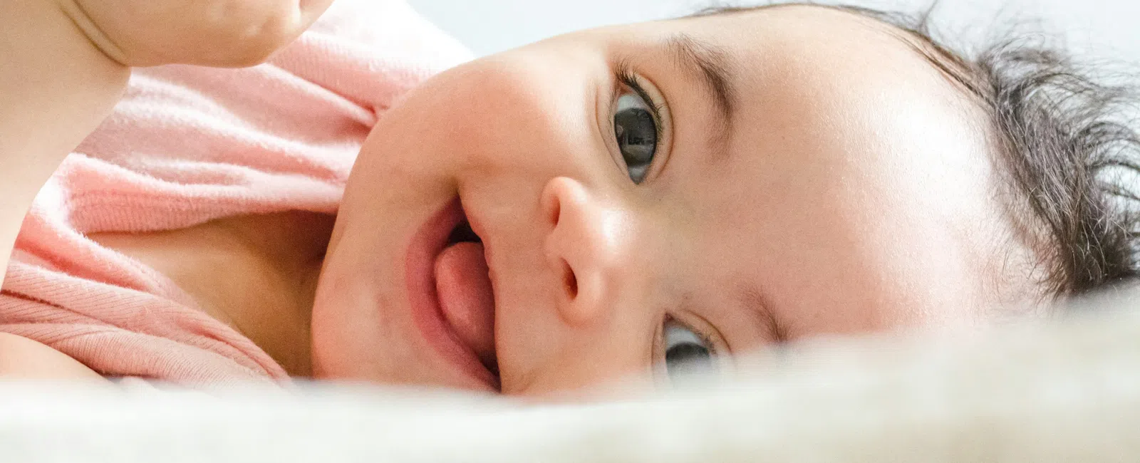 Cute baby lying down smiling with bright eyes and holding a hand, close-up portrait