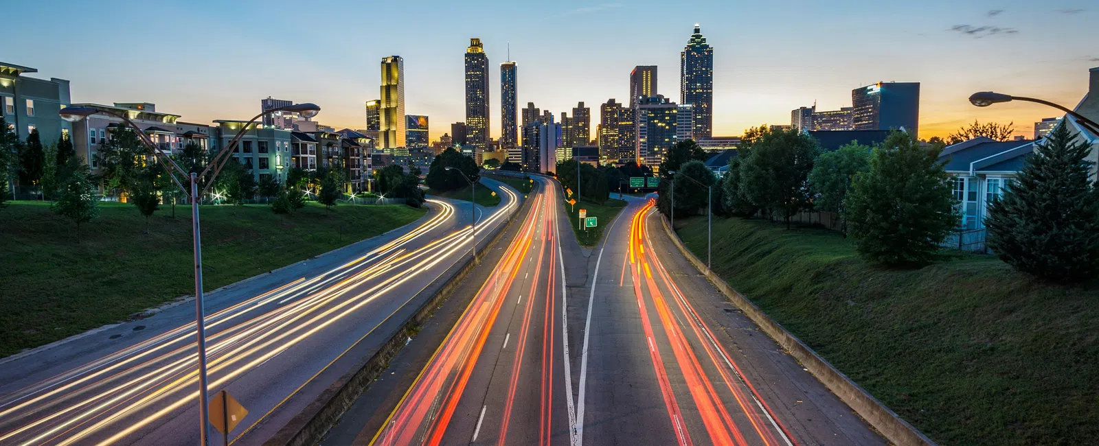 Nighttime city skyline with light trails from cars on a busy highway leading into downtown Atlanta.