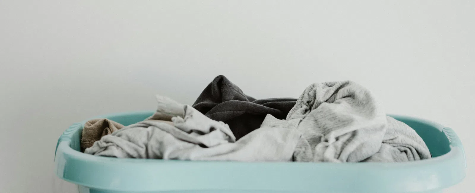 Blue plastic laundry basket filled with various folded and unfolded clothes against a plain white background.