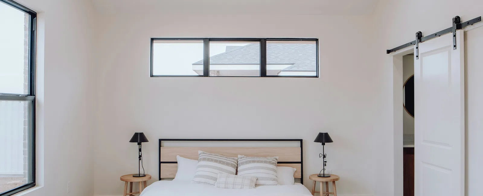 Minimalist bedroom with a bed, beige carpet, ceiling fan, and sliding barn doors in natural light.
