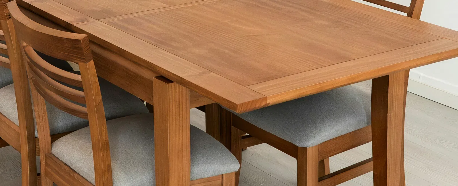 Wooden dining table with six cushioned chairs set on light wood floor in a modern minimalist room.