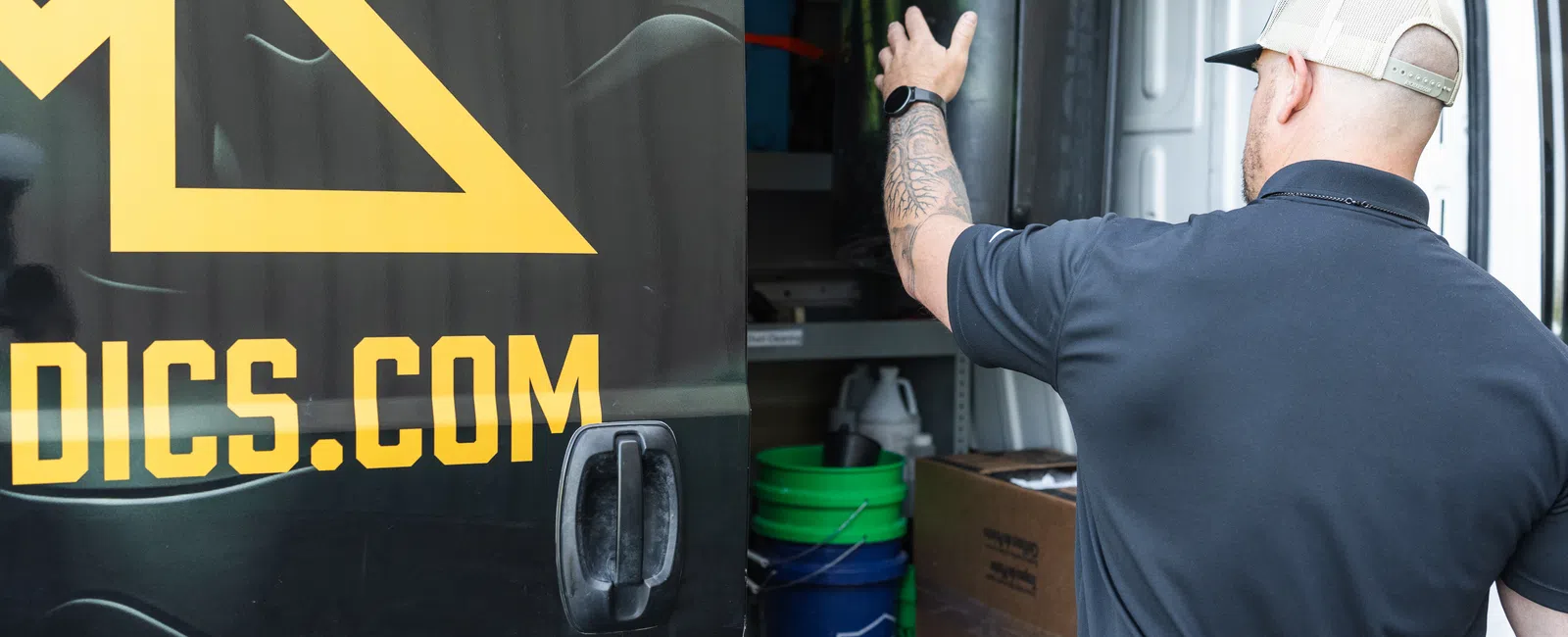 Man in black shirt and beige cap gesturing inside a van with logo on sliding door