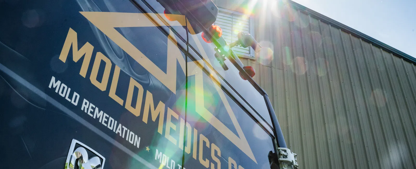 Sunlit black van with MOLMEDICS.COM logo parked outside industrial building under clear blue sky