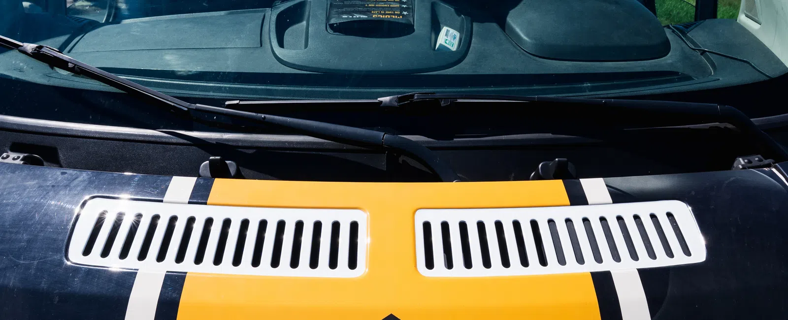 Van front with yellow stripe and black geometric logo on hood under clear blue sky