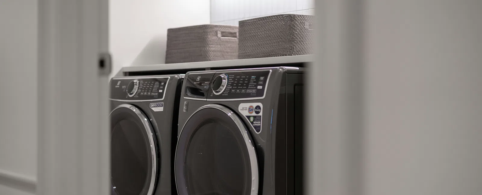 Modern laundry room with black front-load washer and dryer, storage baskets, and overhead cabinets.