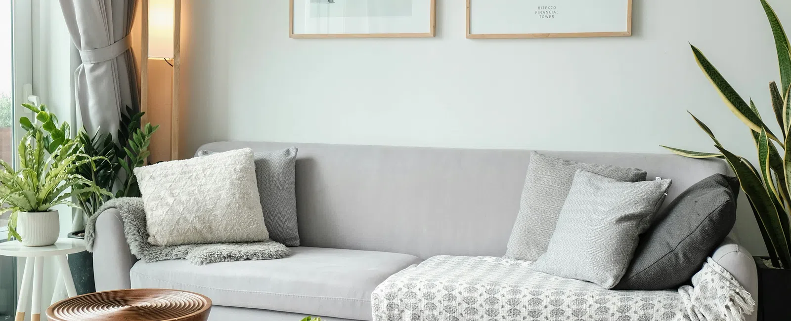 Modern living room with gray sofa, wooden coffee tables, knit pouf, plants, and framed wall art with overlaid text