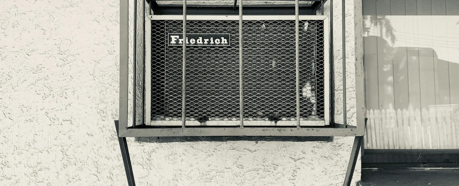 Friedrich air conditioning unit mounted on a textured outdoor wall in black and white.