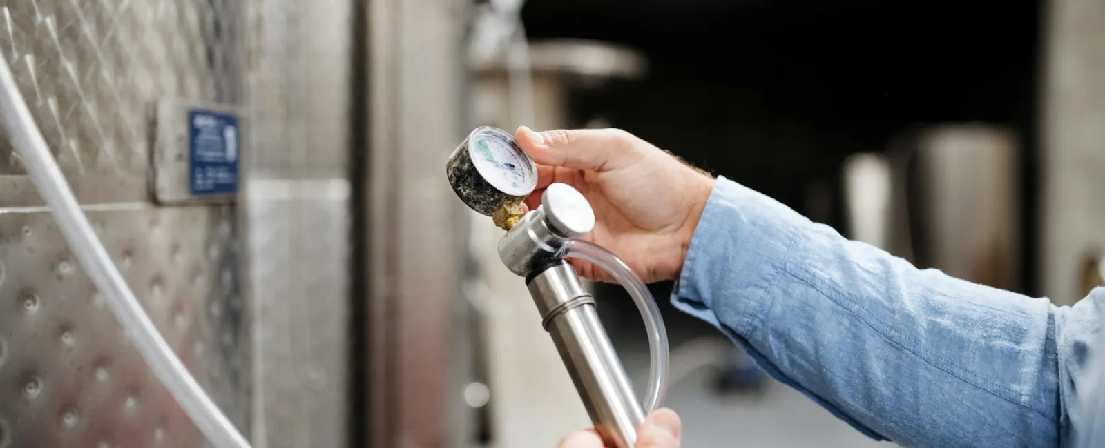 A person adjusts a pressure gauge on equipment in a brewing facility.
