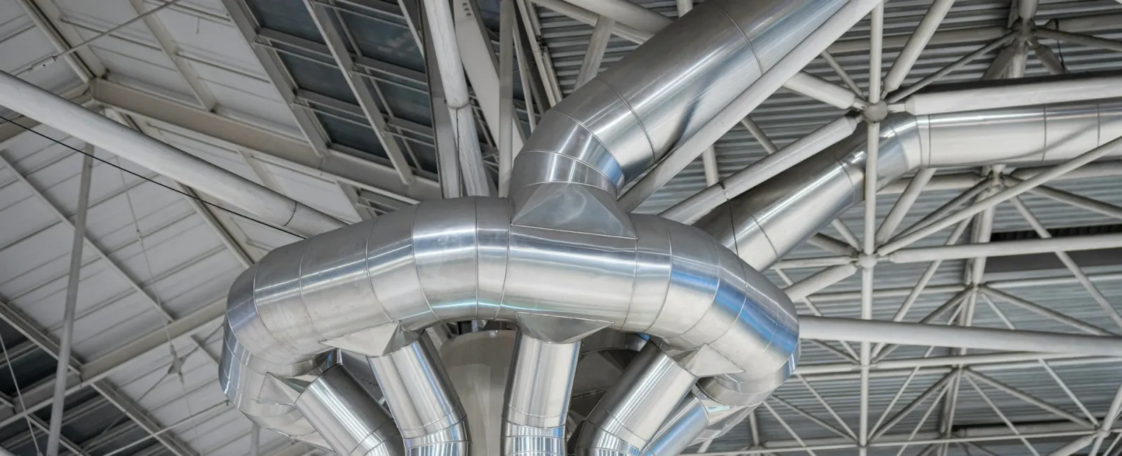 Close-up of industrial metal piping in a large facility ceiling.