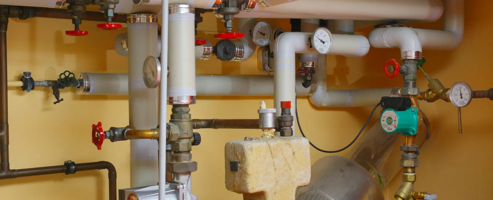 Complex plumbing system with pipes, valves, and gauges in a utility room setting.