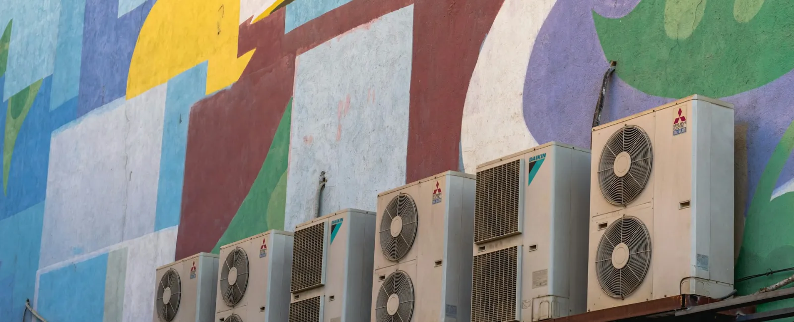 Multiple air conditioning units mounted on a colorful mural background.