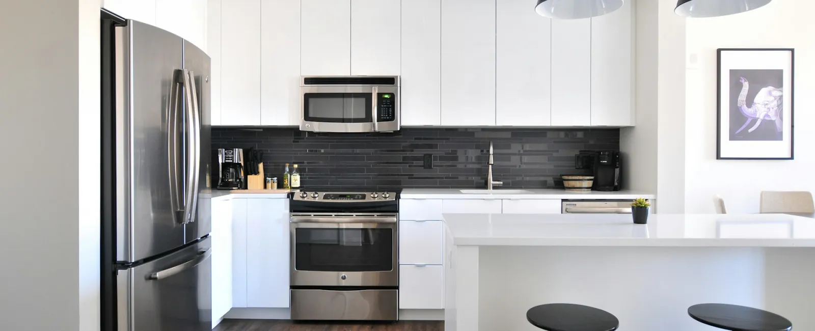 Modern kitchen with sleek stainless steel appliances and black accents, featuring white cabinetry and wooden flooring.