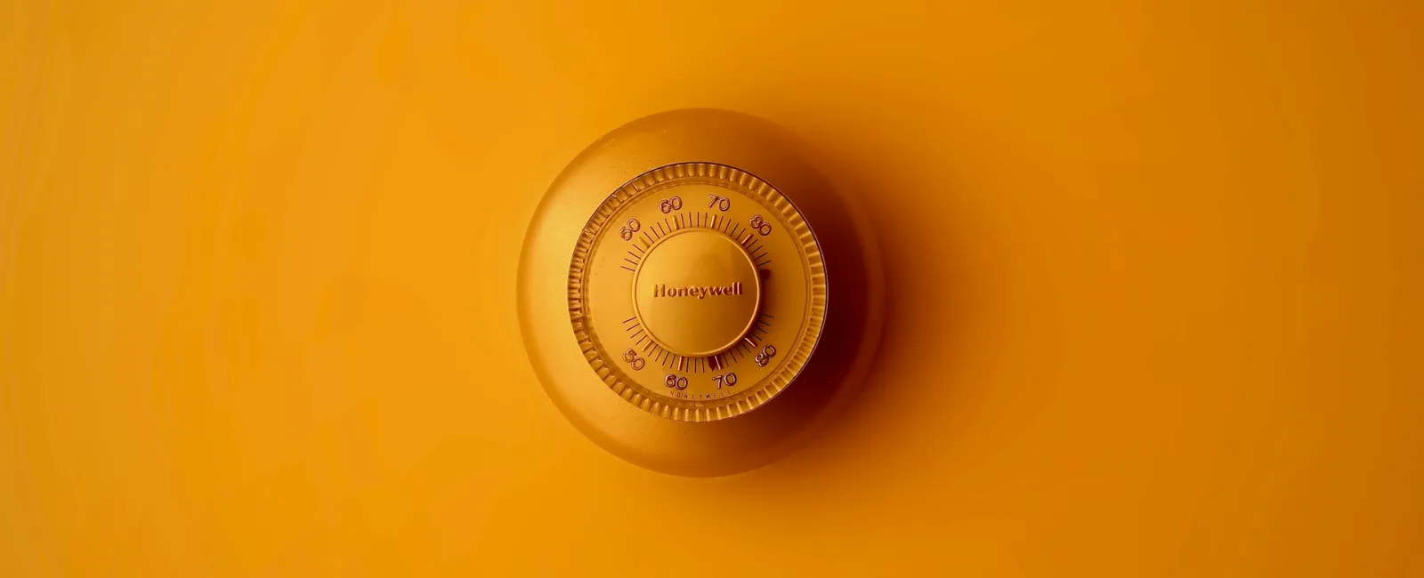 Honeywell thermostat on a bright yellow background, showcasing modern design and functionality.