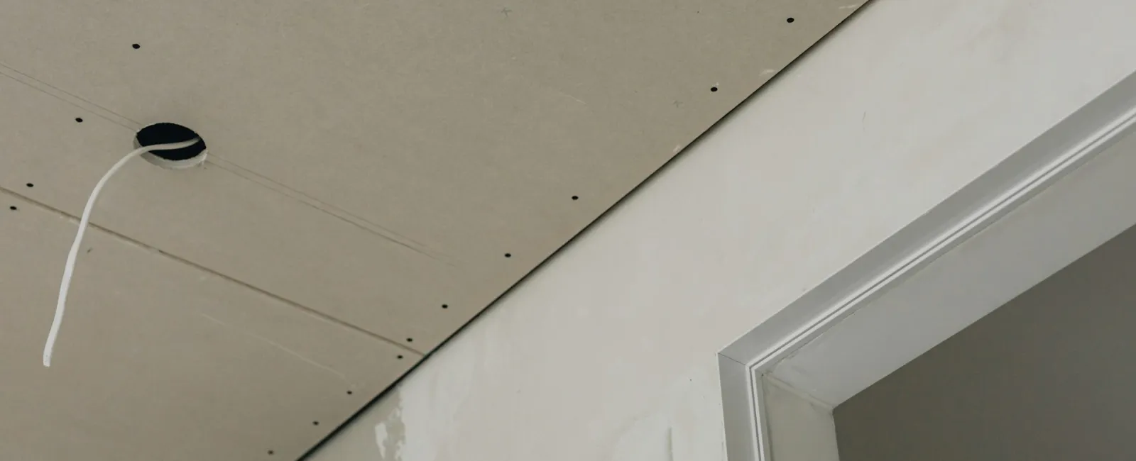 Close-up of drywall installation in a room with an exposed electrical wire.