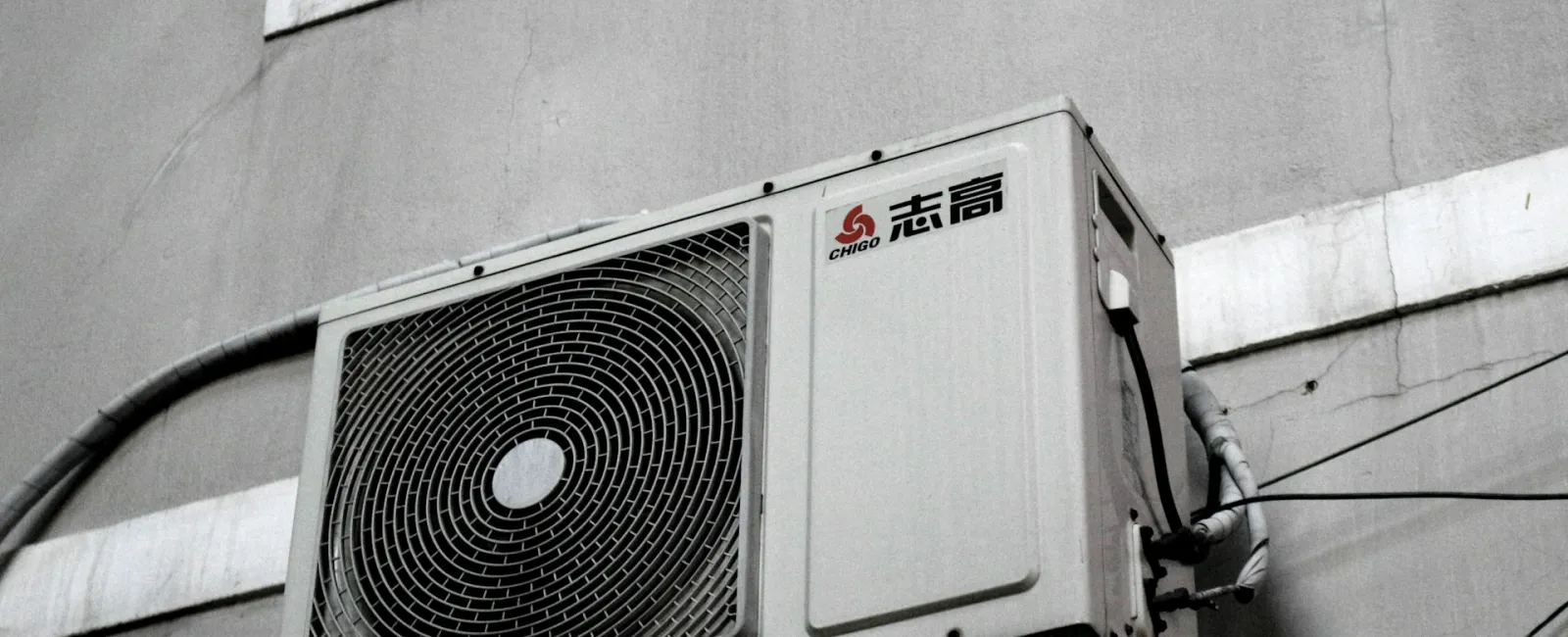 Outdoor air conditioning unit mounted on a building wall, featuring a minimalist design in gray tones.