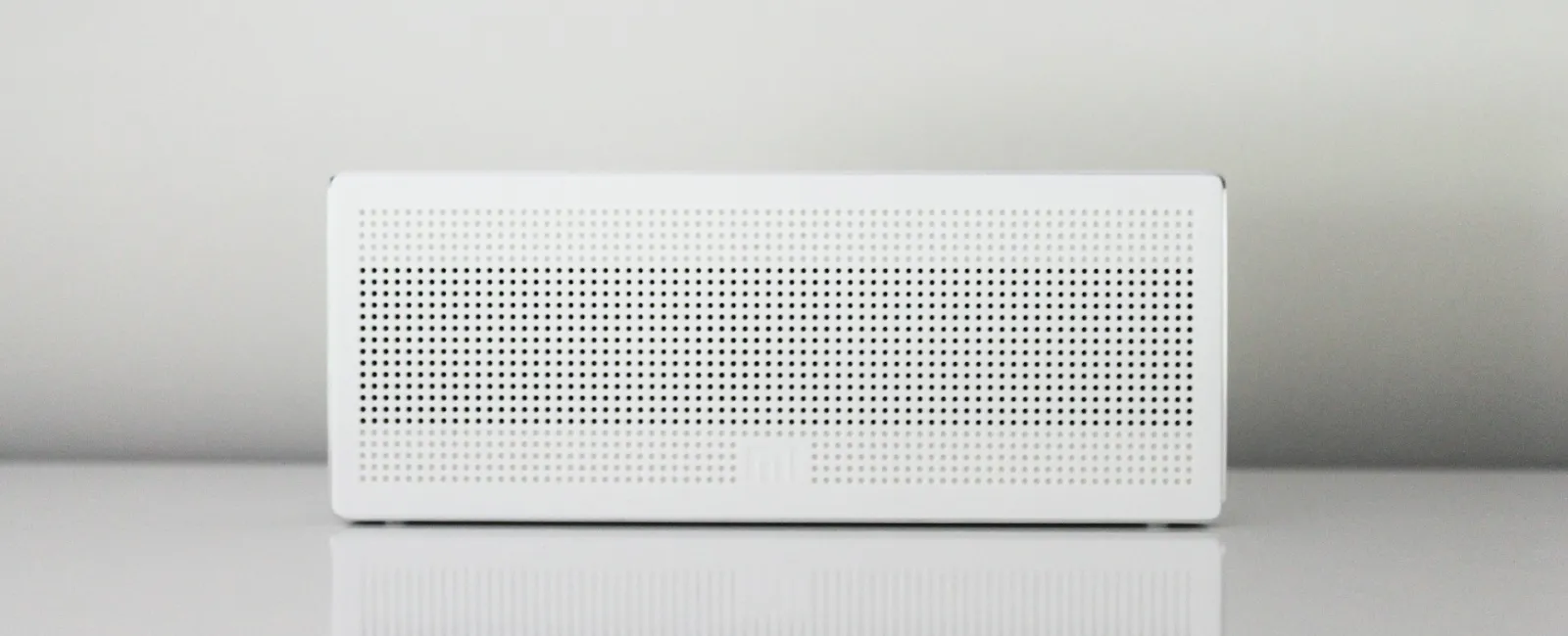 White portable speaker on a reflective surface against a light background.