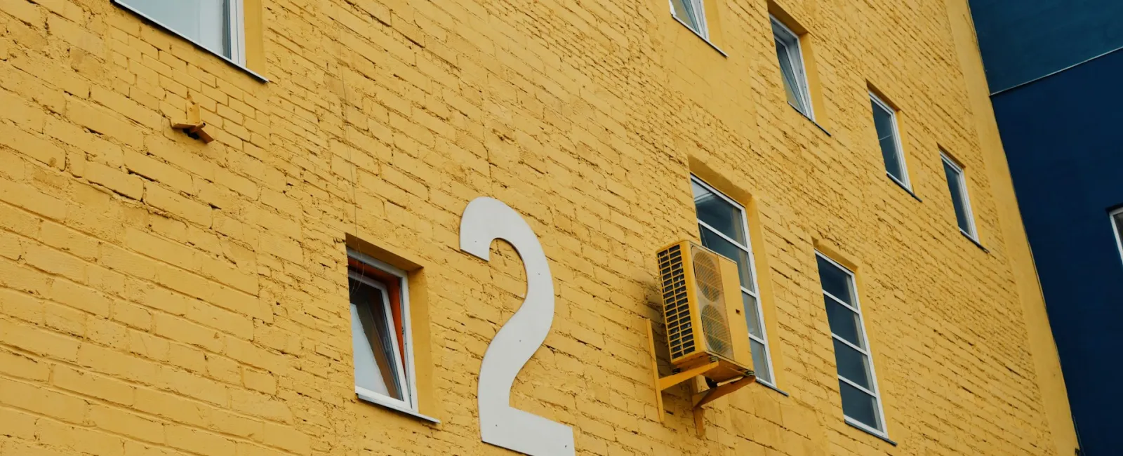Bright yellow building wall with large number two and windows, modern urban architecture.