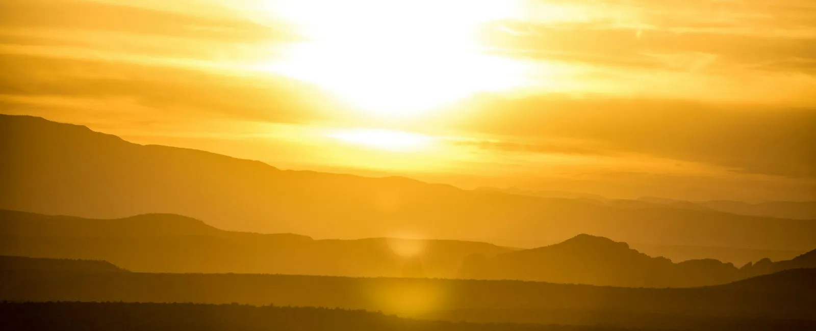 Golden sunset over silhouetted mountains creating a serene landscape scene.