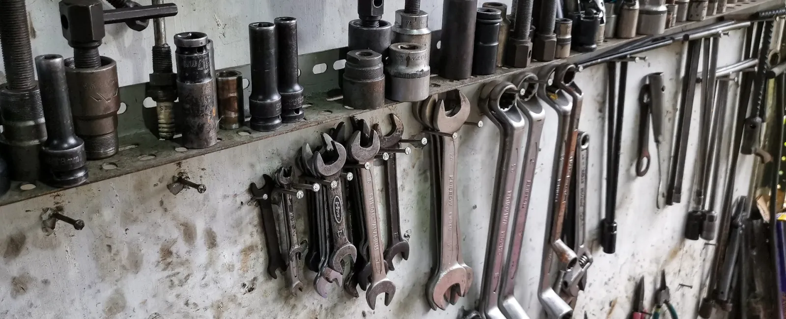 A close-up view of various tools organized on a workshop wall, including wrenches and sockets.