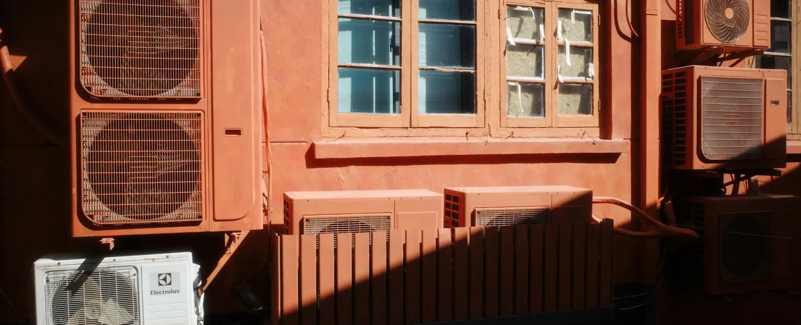 A sunny building wall featuring multiple air conditioning units and a blue window.