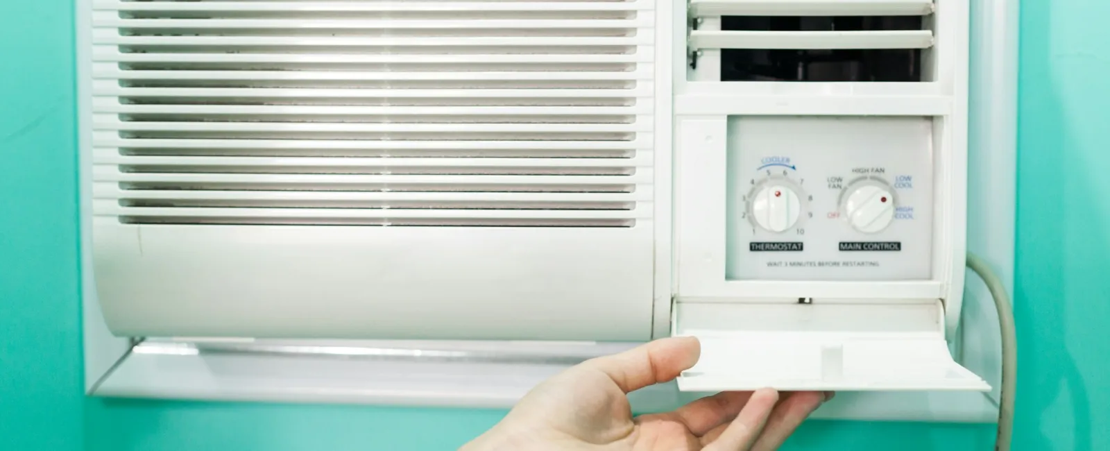 Hand adjusting settings on a white wall-mounted air conditioner with a mint green background.