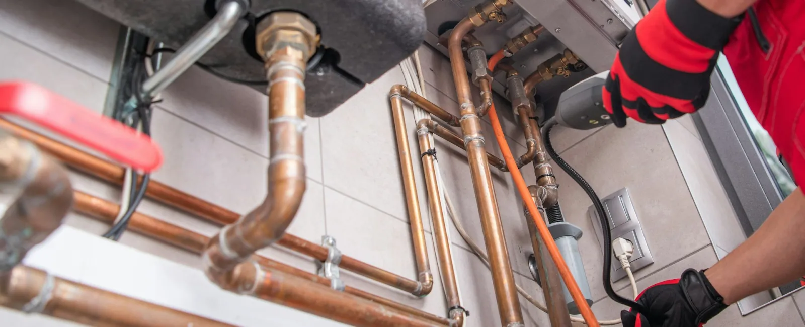 A plumber working on copper pipes and fixtures under a sink, highlighting plumbing repairs.