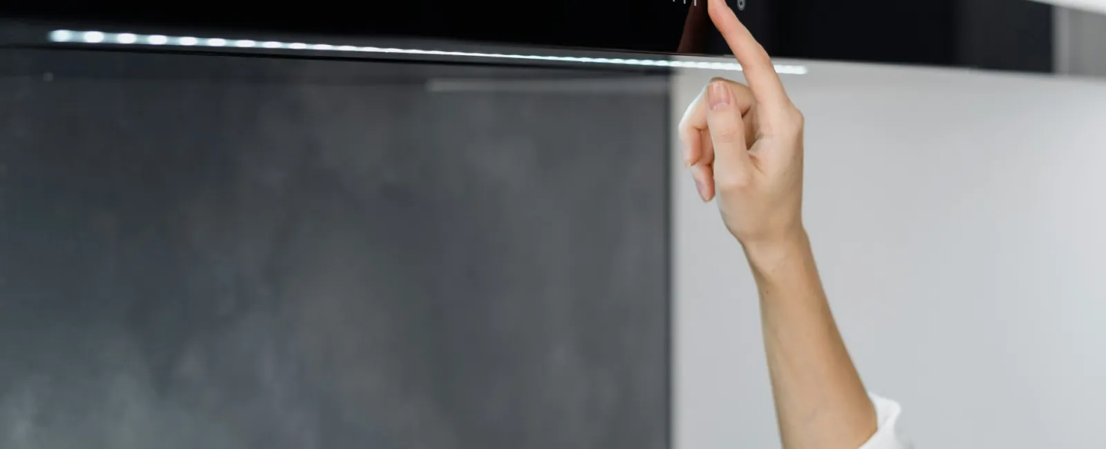 A hand adjusting a sleek black kitchen appliance with modern controls and subtle lighting.
