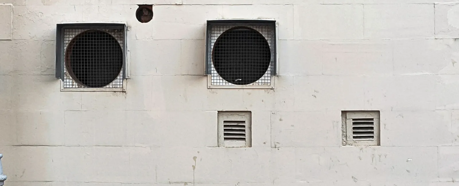 Two circular vents with wire mesh covering on a textured white wall.