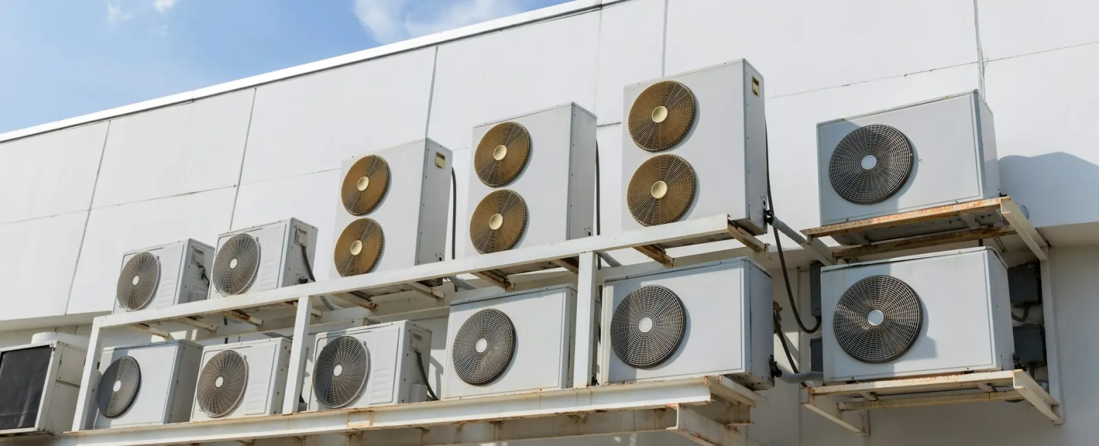 Multiple air conditioning units mounted on a building's exterior under a clear blue sky.