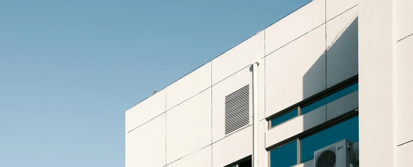 Modern building facade with large windows and air conditioning unit against a clear blue sky.
