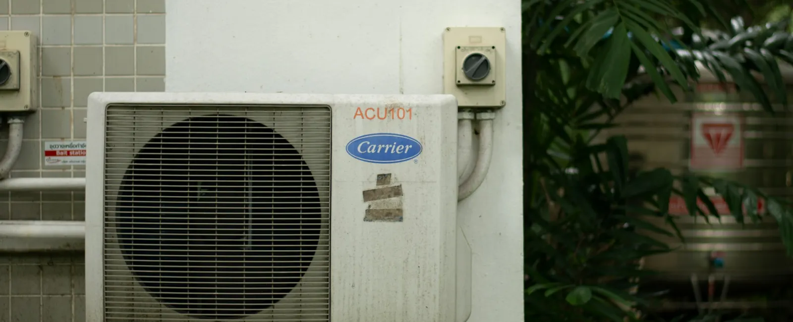 An outdoor air conditioning unit mounted on a wall surrounded by greenery.