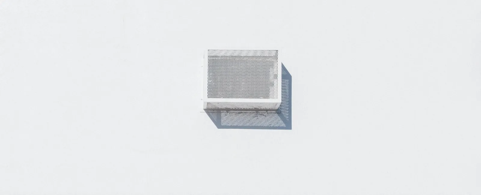 Minimalist architectural detail of a white wall with a rectangular vent casting a soft shadow.