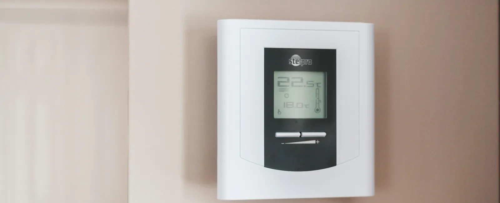 Wall-mounted digital thermostat displaying current and target temperatures in a modern home.