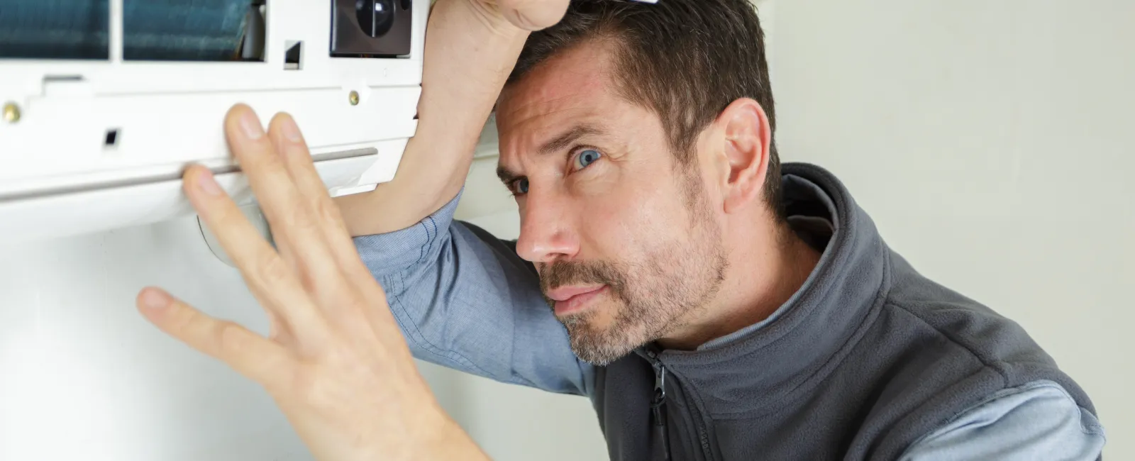 Technician inspecting and repairing a wall-mounted air conditioning unit indoors with focused attention.