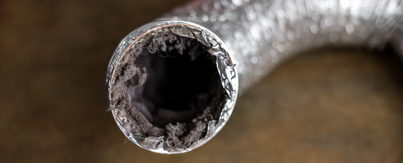 Close-up of a metal dryer vent hose clogged with lint and dust, emphasizing airflow blockage risk.
