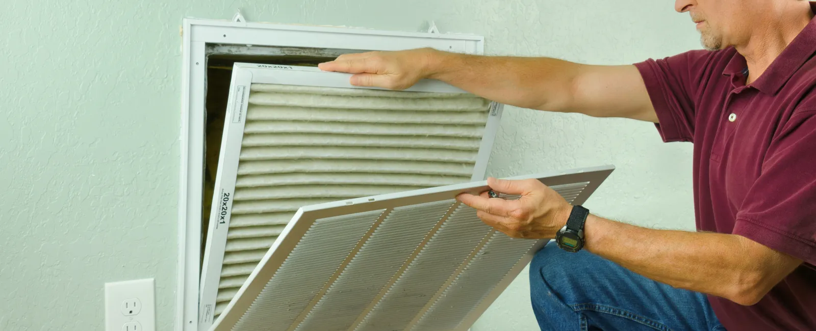A man replacing an air filter in a home ventilation system.