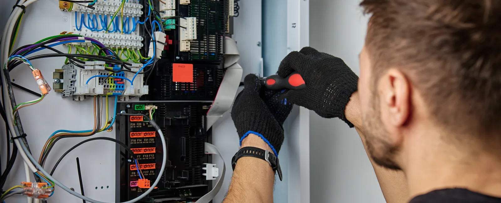 Technician working on electrical control panel with tools and wires in focus.
