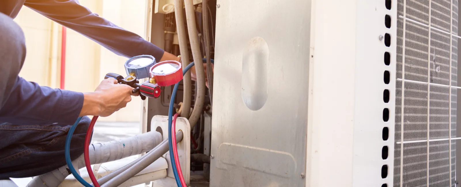 Technician using manifold gauge to check and service large air conditioning unit outdoors on sunny day