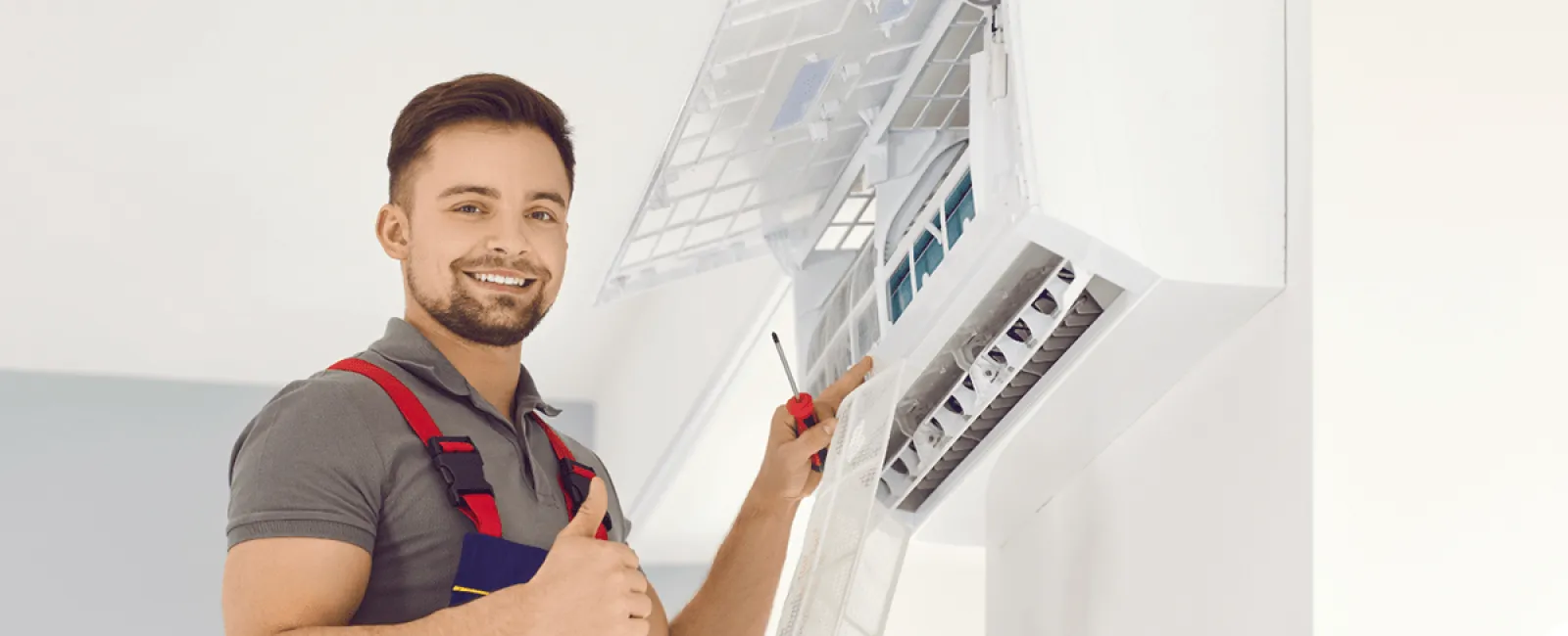 Smiling technician servicing an air conditioning unit with tools in hand, showcasing professionalism and expertise.