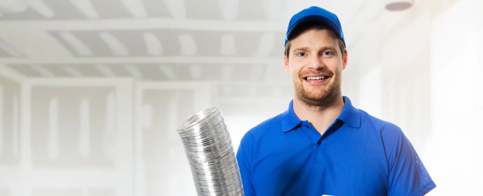 A smiling technician holds ductwork and a vent in a construction space, showcasing HVAC installation tools.