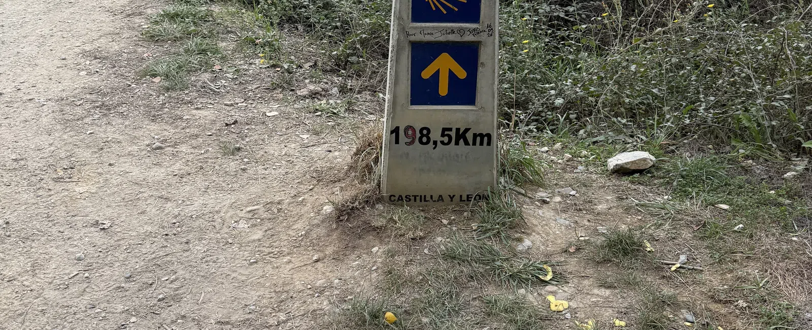 Stone marker on dirt path showing 198.5 km to Santiago de Compostela in Castilla y León on Camino de Santiago trail.