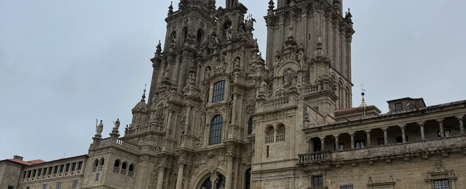 Crowd of tourists visiting the grand historic cathedral with intricate stone facade and twin spires on cloudy day.
