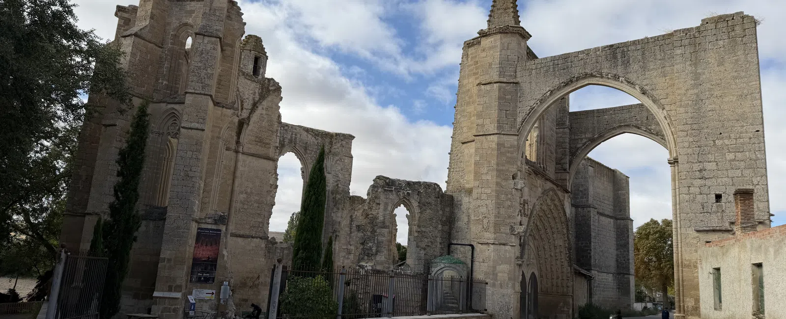 Ancient stone ruins with large arches and gothic windows under a cloudy sky beside a curved road.