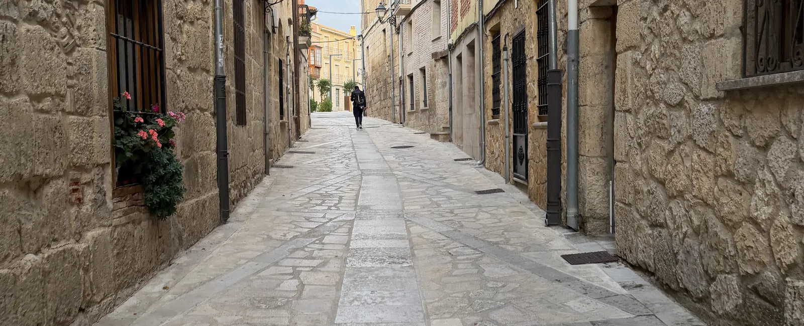 Narrow cobblestone street lined with stone and brick buildings under an overcast sky in a European village.