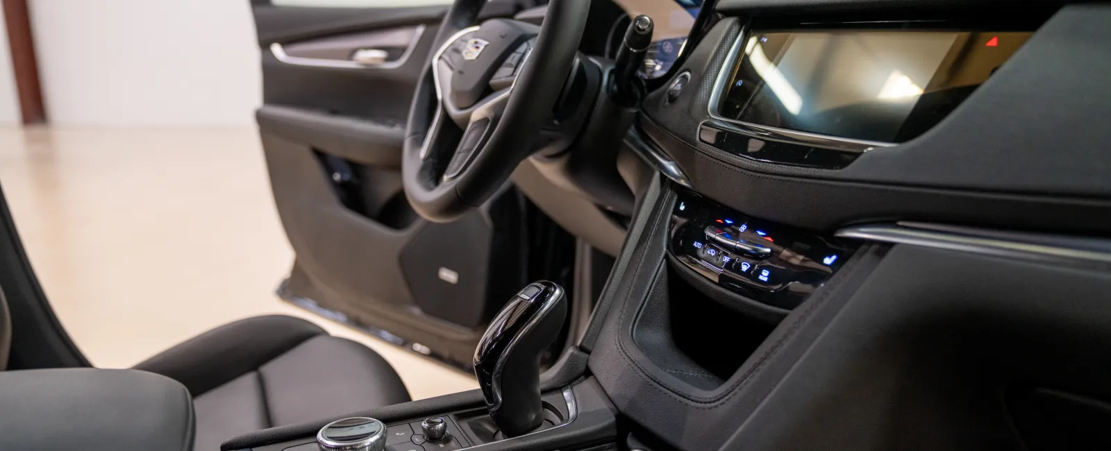 Modern car interior with steering wheel, touchscreen display, gear shift, and black leather seats.