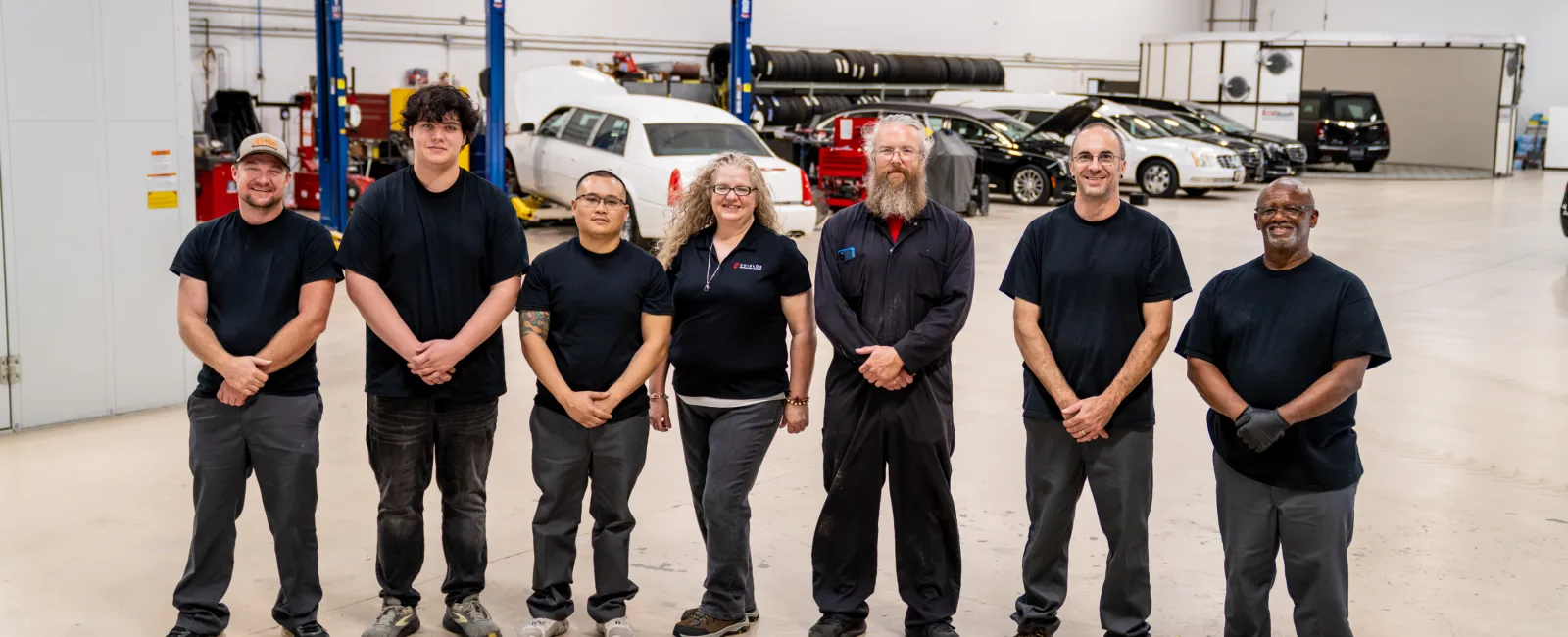Auto repair team standing in a spacious workshop with vehicles and lifts in the background
