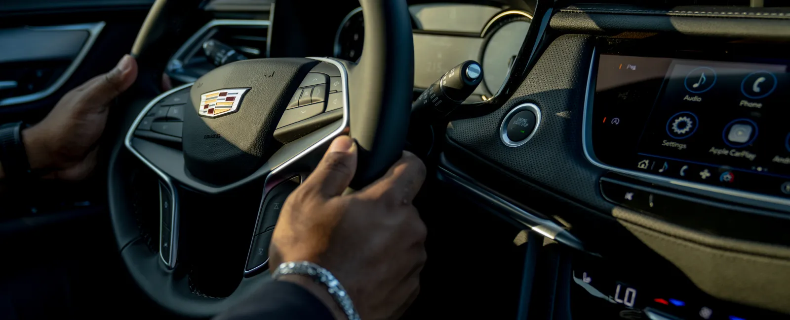 Hands on Cadillac steering wheel with digital dashboard and infotainment system displaying controls and navigation